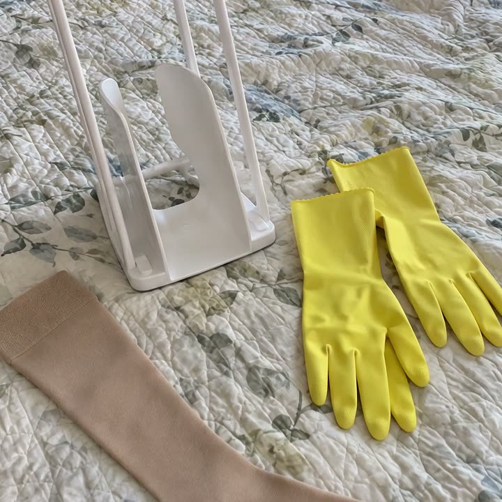A plastic sock aid frame and yellow rubber gloves on a bed